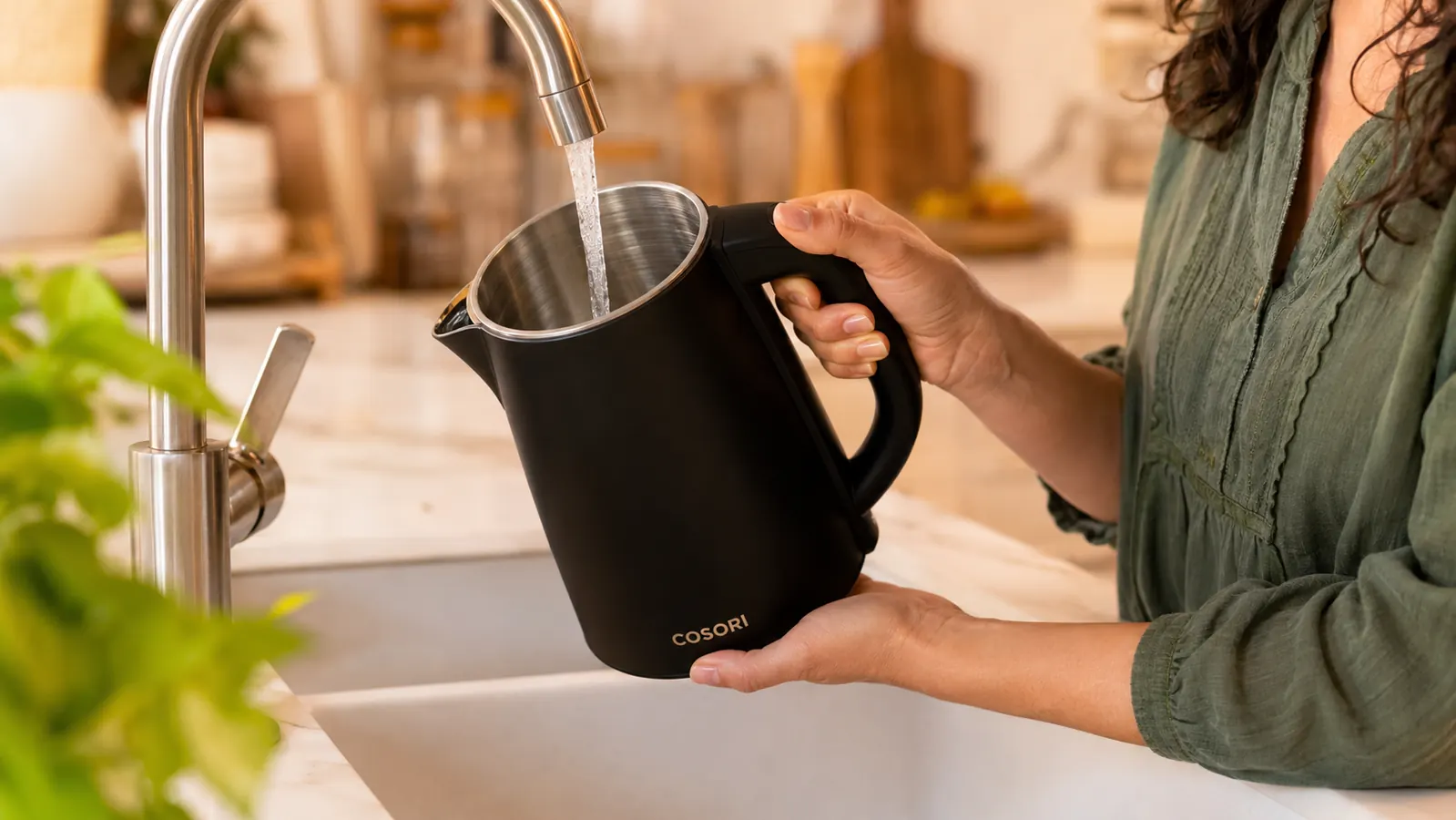 Hand filling the Cosori kettle at the kitchen sink, showing the wide mouth opening