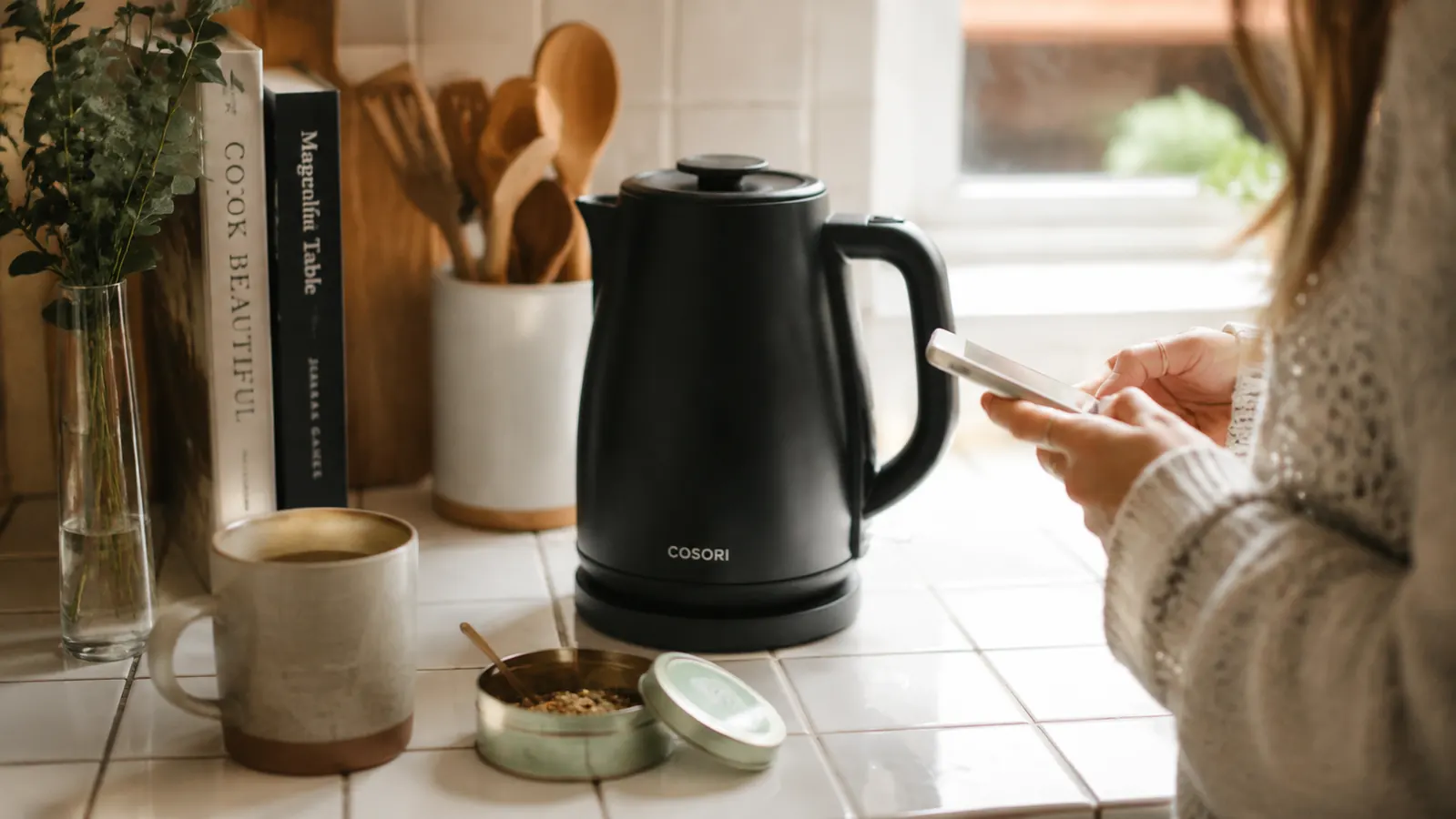 Cosori electric kettle on a small apartment kitchen counter next to a mug and loose-leaf tea tin