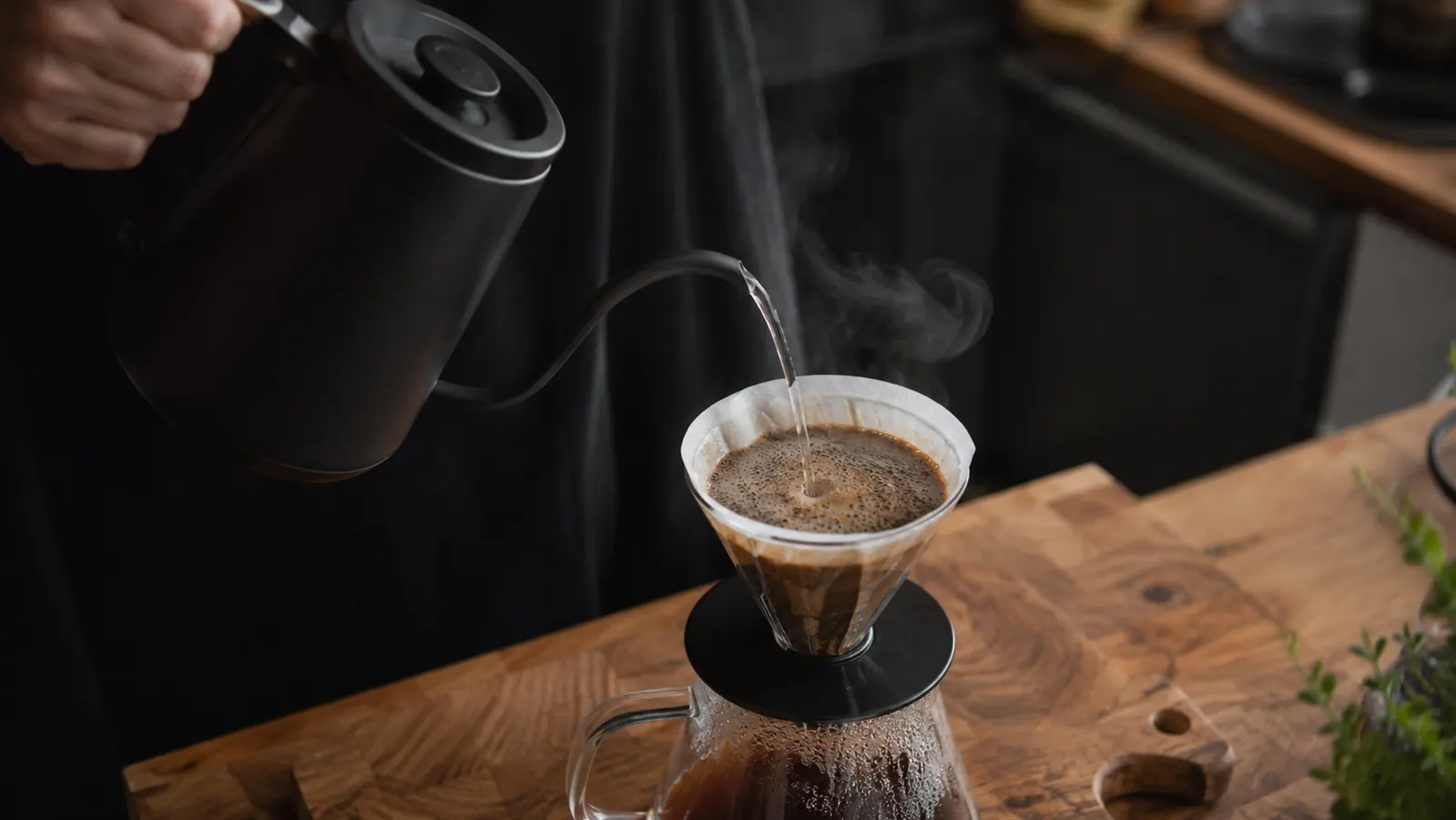 Steam rising from an electric kettle being poured into a pour-over coffee dripper