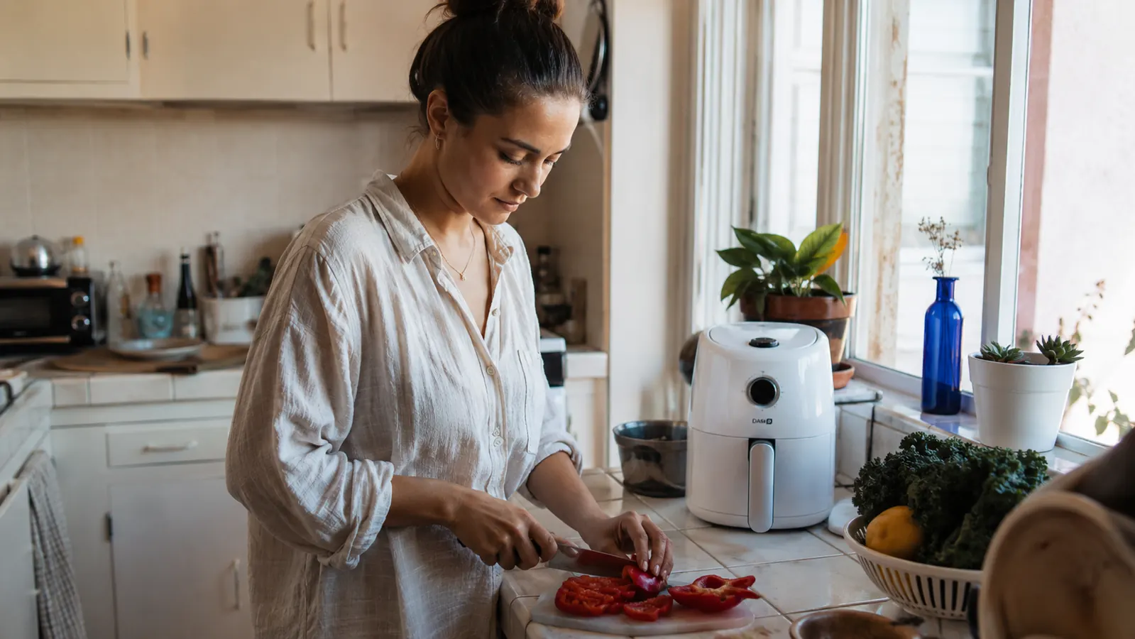 Dash Tasti-Crisp compact air fryer on a small apartment kitchen counter next to a cutting board and vegetables