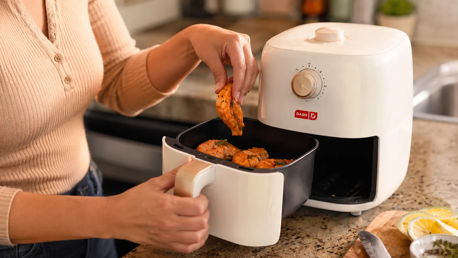 Hand placing frozen chicken tenders into the Dash air fryer basket, non-stick fry basket visible