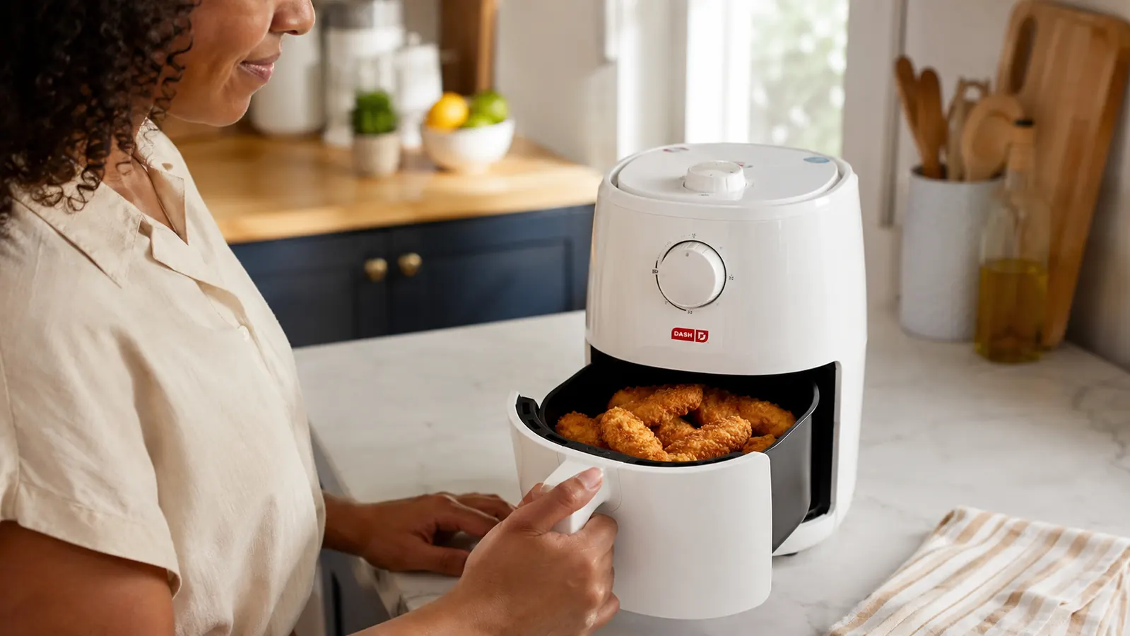 Dash air fryer basket pulled open showing crispy golden chicken tenders inside