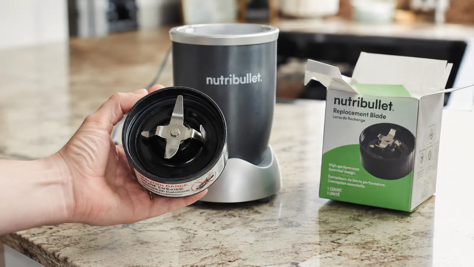 Person holding a NutriBullet replacement blade assembly next to the motor base, showing the part is available separately